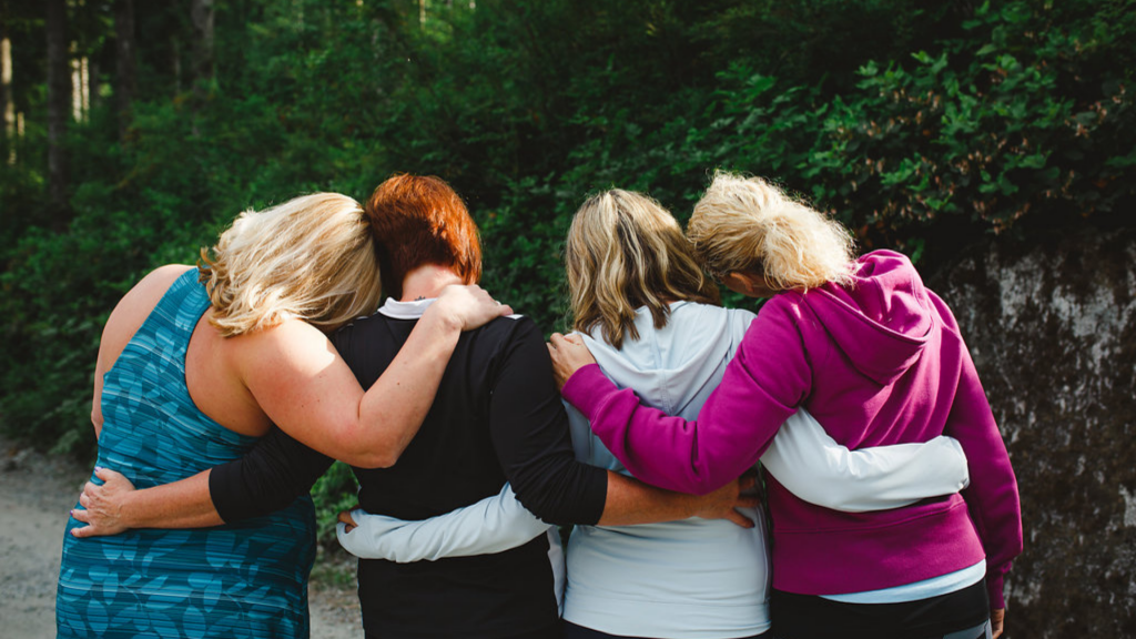 a group of women with arms around each other facing their backs in the forest for the uBlossom Kindness Project