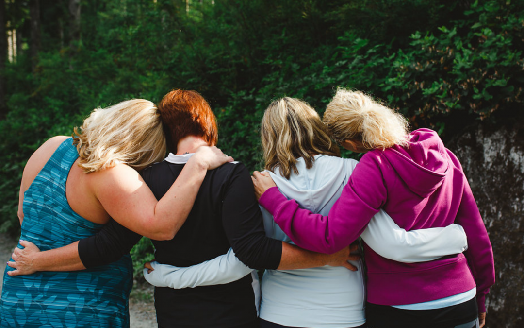 a group of women with arms around each other facing their backs in the forest for the uBlossom Kindness Project